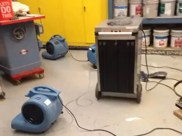 Dehumidifier and air movers drying a basement workshop floor