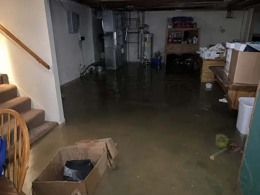 Standing water across a basement floor at the foot of the stairs