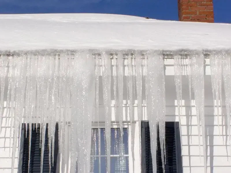 Heavy icicles along a snow-loaded roof edge above a row of windows